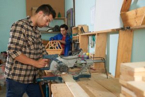 side-view-man-plaid-shirt-sawing-wood-timber-workshop_1098-19111